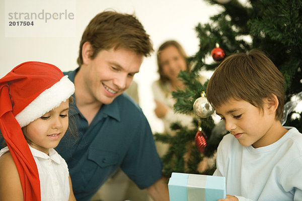 Vater und zwei Kinder am Weihnachtsbaum sitzend  Tochter mit Weihnachtsmütze  Sohn Eröffnungsgeschenk