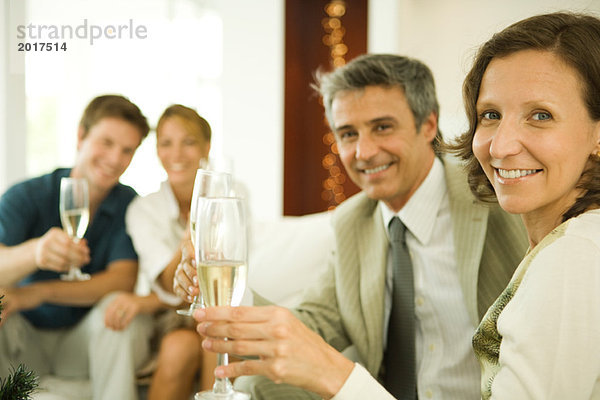 Paar macht einen Toast mit Champagner  lächelt in die Kamera  Freunde im Hintergrund