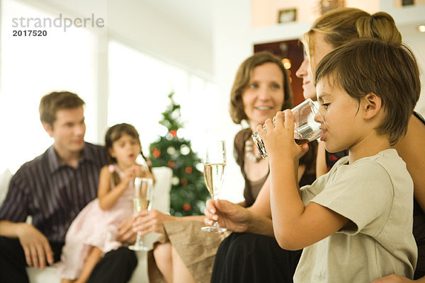 Junge trinkendes Getränk  Erwachsene trinken Champagner  Weihnachtsbaum im Hintergrund