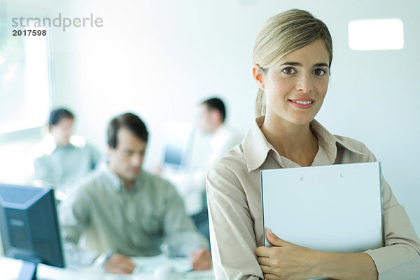 Junge Geschäftsfrau hält Laptop vor der Brust im Büro  lächelt in die Kamera  Porträt