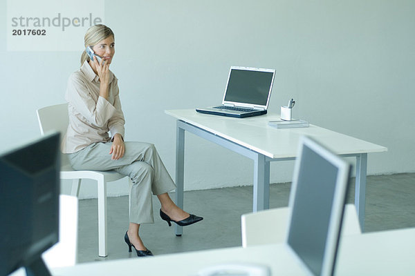Geschäftsfrau am Schreibtisch sitzend  mit Handy  volle Länge