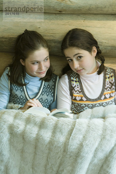 Zwei Teenagermädchen in Winterkleidung sitzen unter warmer Decke zusammen