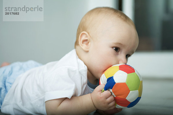 Baby auf dem Boden  hält den Ball bis zum Mund.