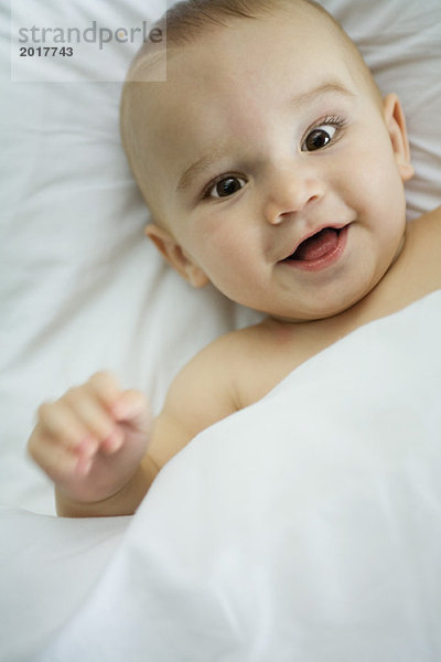 Baby im Bett  unter der Decke  lächelnd vor der Kamera