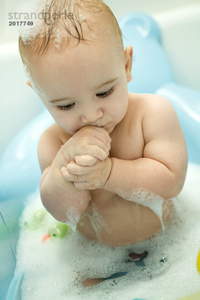 Baby badet in schäumendem Wasser  hält die Hände hoch.