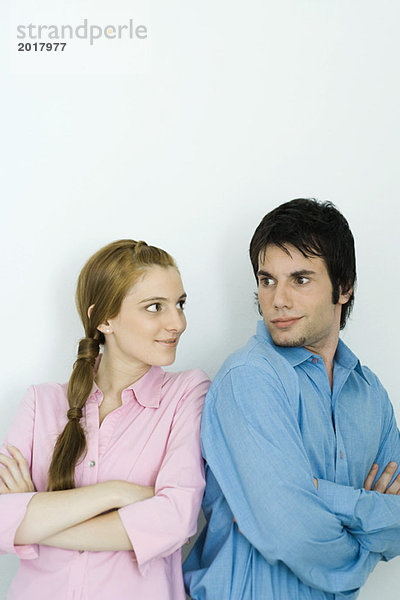 Ein junges Paar schaut sich über die Schultern  die Arme gefaltet.