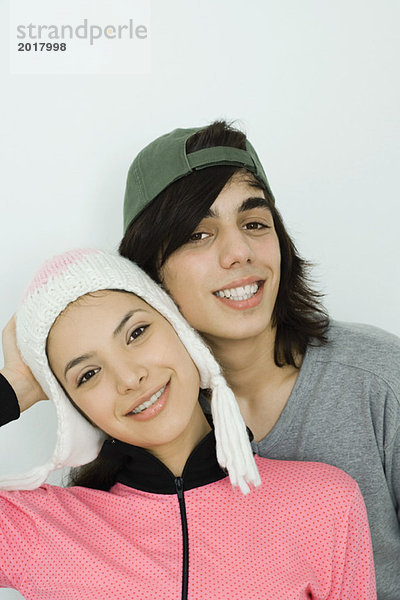 Junges Paar lächelt gemeinsam in die Kamera  beide mit Hut  Wange an Wange  Portrait