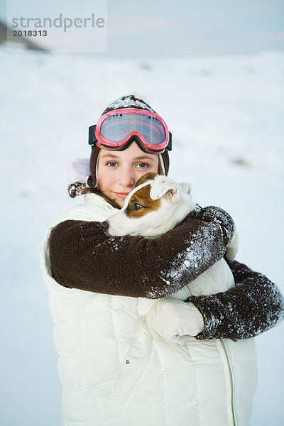 Teenagermädchen umarmt Hund  in Winterkleidung  lächelnd vor der Kamera  Portrait