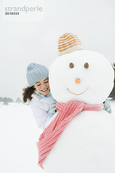 Junge Frau umarmt Schneemann  lächelnd  Augen geschlossen  Portrait