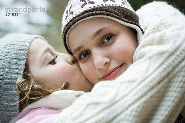 Teenager Mädchen lächelt in die Kamera  Schwester küsst sie auf die Wange  Portrait
