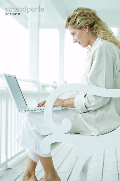 Frau auf der Veranda sitzend  mit Laptop  Seitenansicht