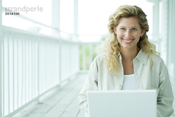 Frau mit Laptop auf der Veranda  lächelt in die Kamera  Porträt