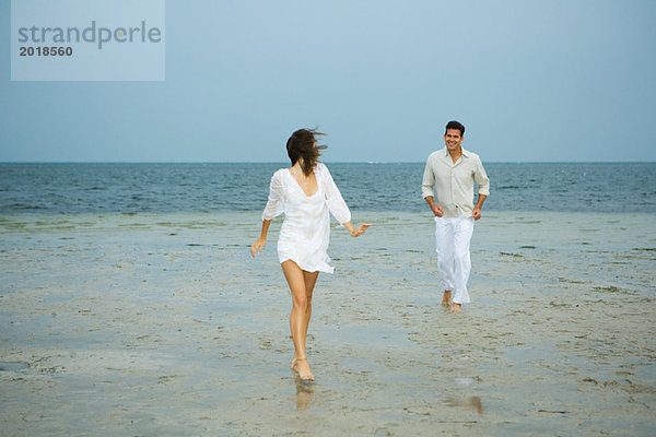 Mann und junge Begleiterin am Strand  auf Kamera zugehen  Mann im Hintergrund  volle Länge