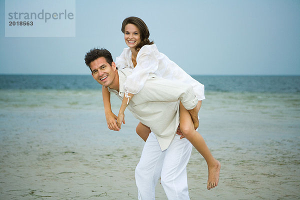 Mann mit junger weiblicher Begleiterin am Strand  lächelnd vor der Kamera