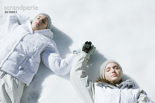 Teenagermädchen auf Schnee liegend mit geschlossenen Augen  Händchen haltend