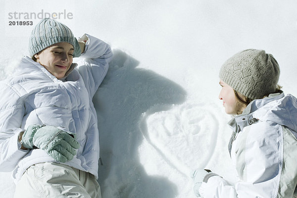 Teenagermädchen auf Schnee liegend  Herz mit Initialen auf Schnee gezeichnet