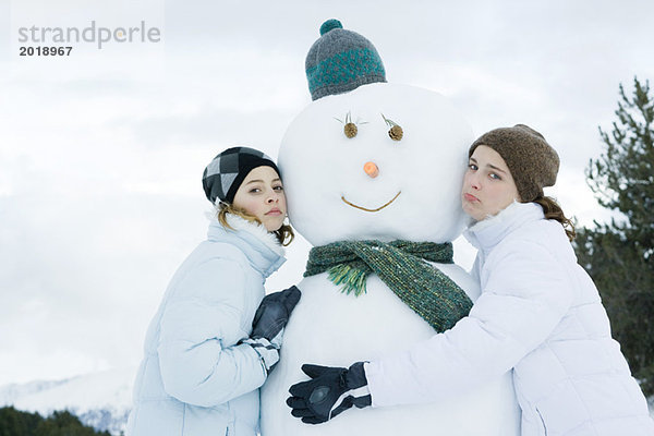 Teenagermädchen lehnen sich gegen den Schneemann.