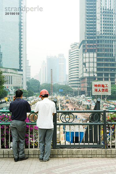 China  Provinz Guangdong  Guangzhou  zwei Männer schauen über die Baustelle  Rückansicht