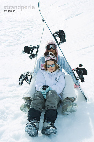 Zwei junge Skifahrer sitzen unter den Skiern  lächeln vor der Kamera  Porträt