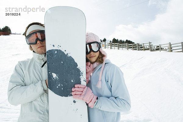 Teenagerin und junger Mann stehen zusammen  halten Snowboard  lächeln in die Kamera  Porträt