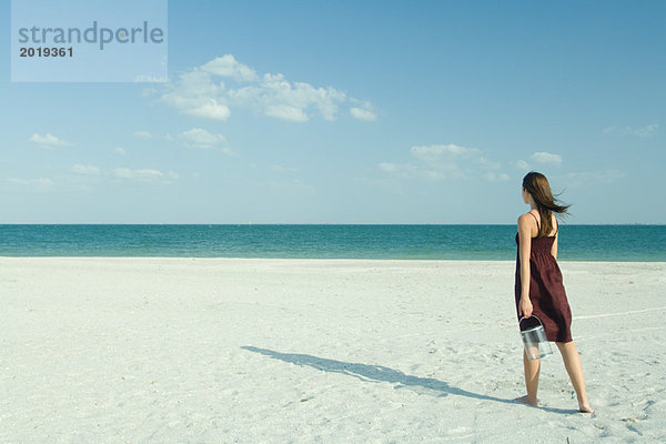 Frau geht über den Strand  trägt transparenten Behälter  volle Länge  Rückansicht