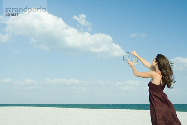 Frau steht am Strand  hält klaren Behälter hoch  löst Wolken  optische Täuschung