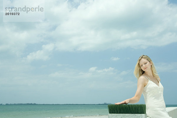 Frau sitzt in der Nähe des Meeres  berührt Weizengrashalme