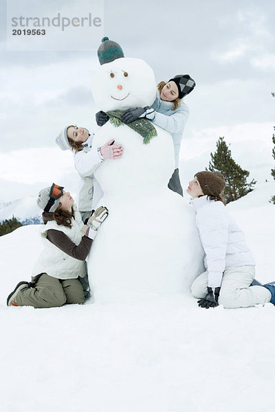 Junge Freundinnen um den Schneemann gruppiert