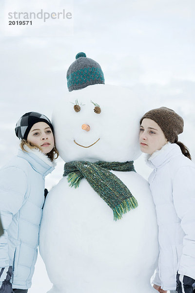 Zwei junge Mädchen  die sich gegen den Schneemann lehnen.