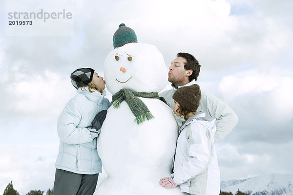 Drei junge Freunde küssen Schneemann