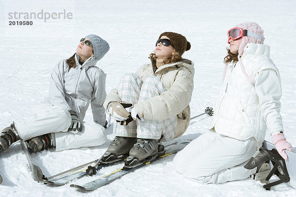 Drei jugendliche Skifahrerinnen sitzen im Schnee und tragen eine Sonnenbrille.