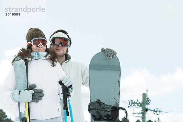 Junges Paar in Skibekleidung  Mann mit Snowboard  Frau mit Skistöcken