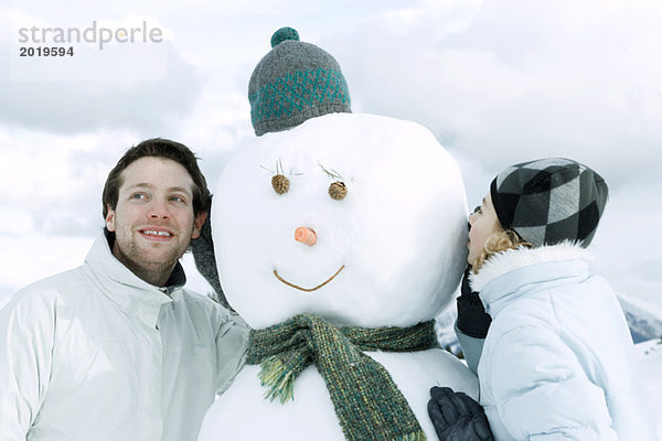 Zwei junge Freunde auf der anderen Seite des Schneemanns  der eine flüstert  der andere lauscht.