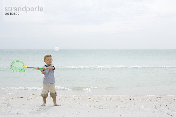 Kleiner Junge am Strand stehend  Fangball mit Netz  volle Länge