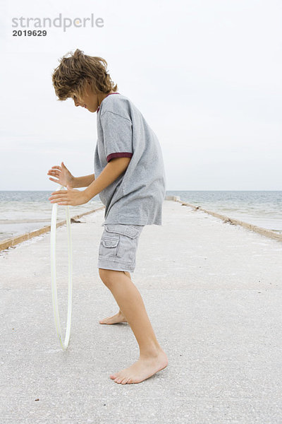 Junge steht auf dem Pier  spielt mit Kunststoffreifen  Seitenansicht  volle Länge