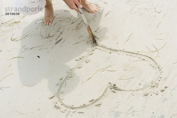 Mann verfolgt Herz in Sand mit Stock  Hochwinkelansicht  Ausschnittansicht