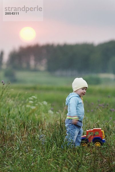 Ein kleiner Junge steht mit einem Spielzeug-LKW auf einem Feld.