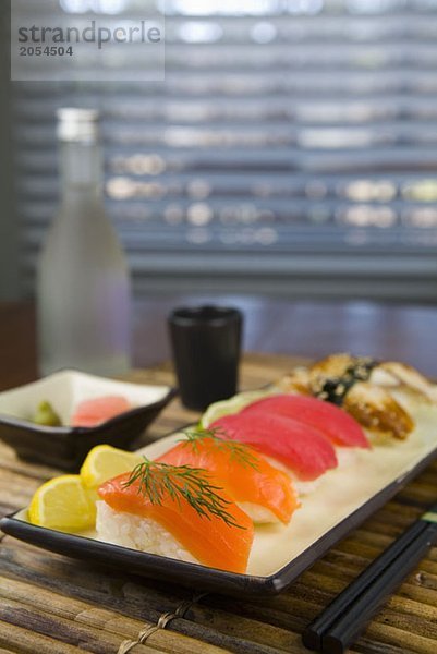Nigiri-Sushi neben Gewürzen  einer Tasse und einer Flasche Sake
