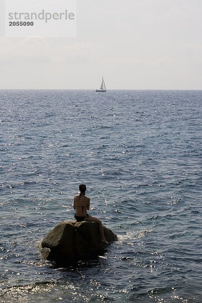 Eine Frau sitzt auf einem Felsen im Meer.