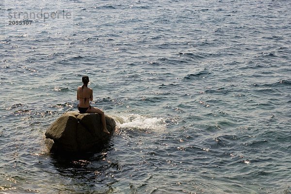 Eine Frau sitzt auf einem Felsen im Meer.