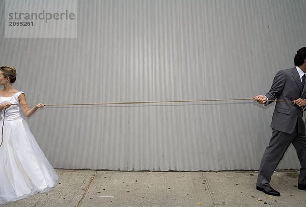 Eine Braut und ein Bräutigam ziehen ein Seil in verschiedene Richtungen.