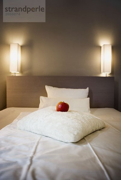 Ein roter Apfel auf einem weißen Kissen auf einem Bett