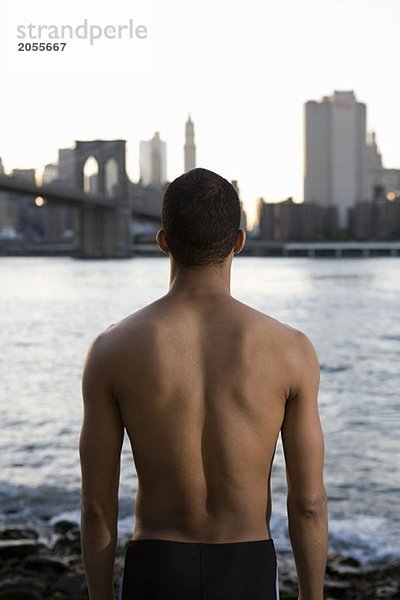 Ein halbgekleideter Mann  der über den Fluss nach Manhattan schaut.