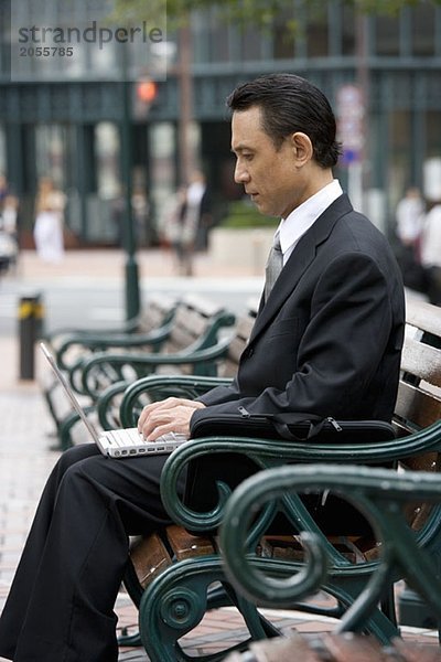 Ein Geschäftsmann  der auf einer Bank sitzt und seinen Laptop benutzt.