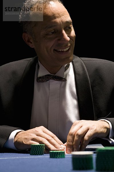 Gut gekleideter Mann lächelnd beim Kartenspielen am Kasinotisch