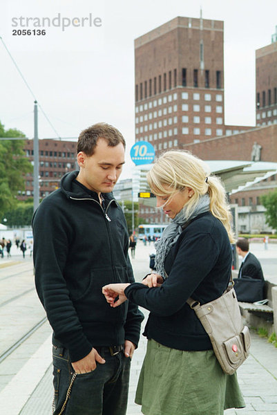 Paar schaut auf die Uhr an der Straßenbahnhaltestelle