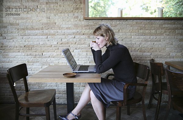 Eine Frau sitzt im Café am Laptop und trinkt einen Kaffee