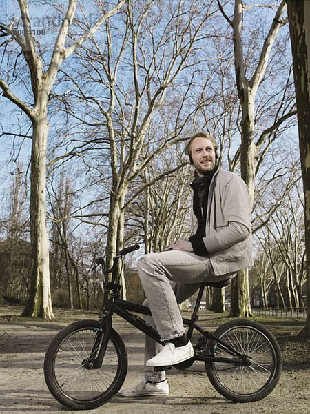 Ein Mann  der Kopfhörer trägt und auf einem BMX im Park sitzt.