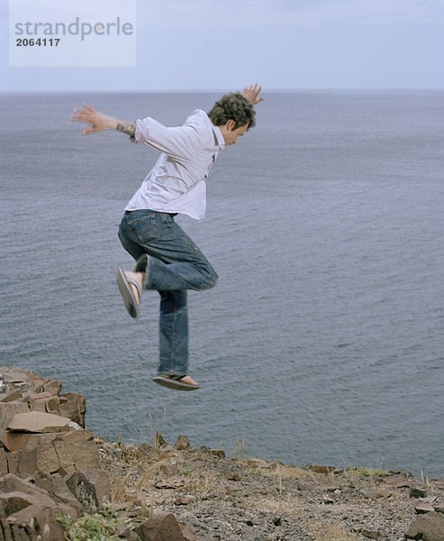 Ein Mann  der von einer Klippe in der Nähe des Meeres springt.