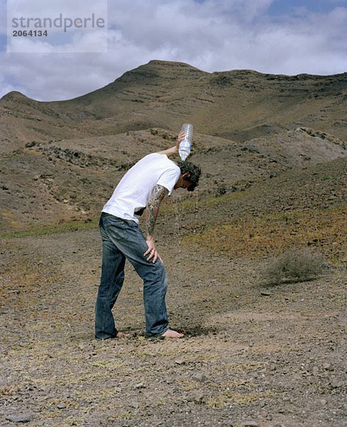Ein Mann  der in einer trockenen Landschaft steht und Wasser über den Kopf schüttet.